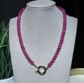 A handcrafted fuschia beaded necklace with a gold sailor clasp, displayed on a  jewelry bust.