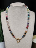 A multi gem handcrafted beaded necklace with a gold sailor clasp, displayed on a  jewelry bust.