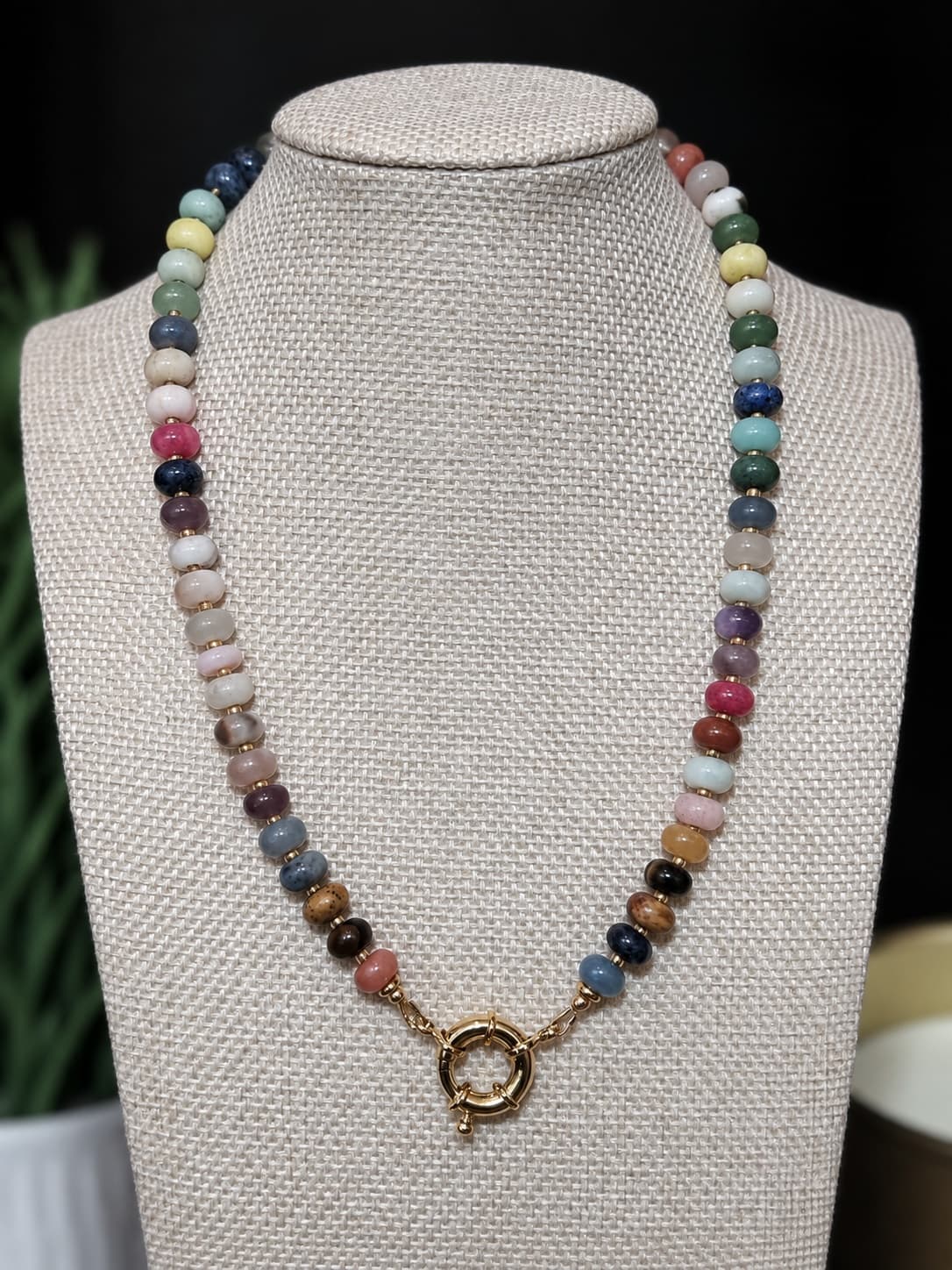 A multi gem handcrafted beaded necklace with a gold sailor clasp, displayed on a  jewelry bust.